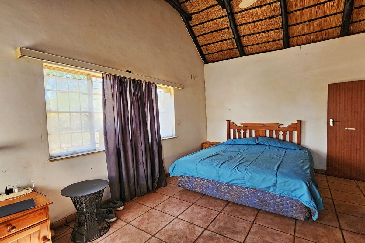 A bedroom featuring a high thatched roof with exposed timber rafters, tiled flooring, and a built-in cupboard.
