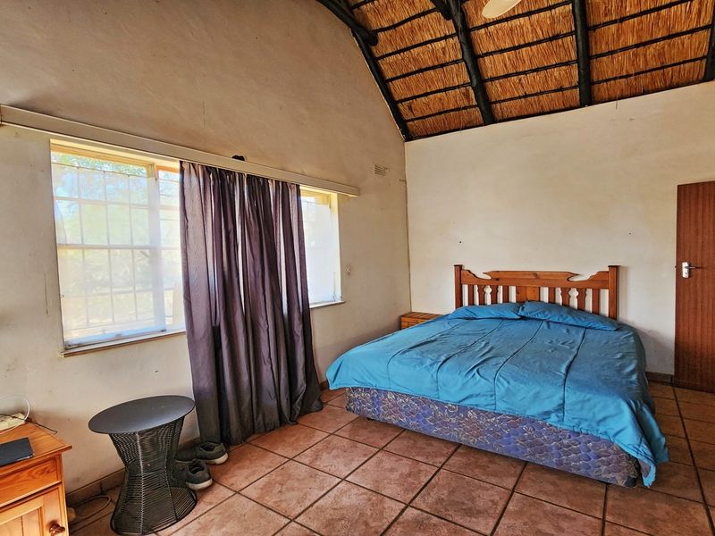 A bedroom featuring a high thatched roof with exposed timber rafters, tiled flooring, and a built-in cupboard.