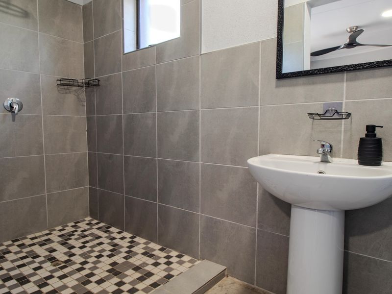 Modern bathroom featuring a walk-in shower with mosaic floor tiles, large format wall tiles, and a white pedestal basin.