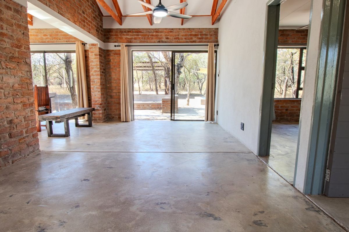 Spacious living area featuring exposed brick walls, timber rafters, polished concrete floors, and large sliding doors opening to the outdoor space.
