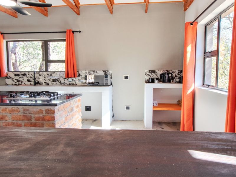 A rustic-style kitchen featuring exposed timber beams, a brick-based island with a granite countertop, gas hob, and tiled backsplash with ample natural light.