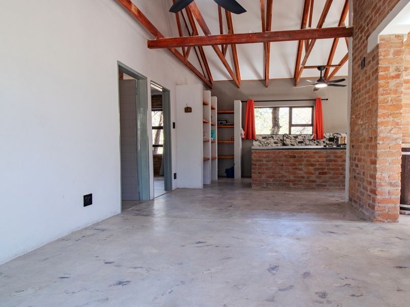 Spacious open-plan living area featuring exposed timber roof trusses, polished concrete floors, and a rustic brick kitchen counter.