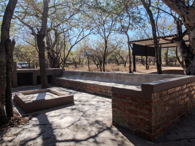 Outdoor patio area featuring built-in brick seating and a central fire pit, set within a natural, wooded environment.