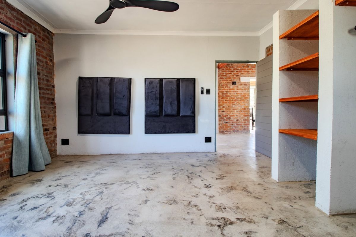 Spacious bedroom featuring industrial-style exposed brick walls, polished concrete floors, and built-in shelving, offering a modern and minimalist aesthetic.
