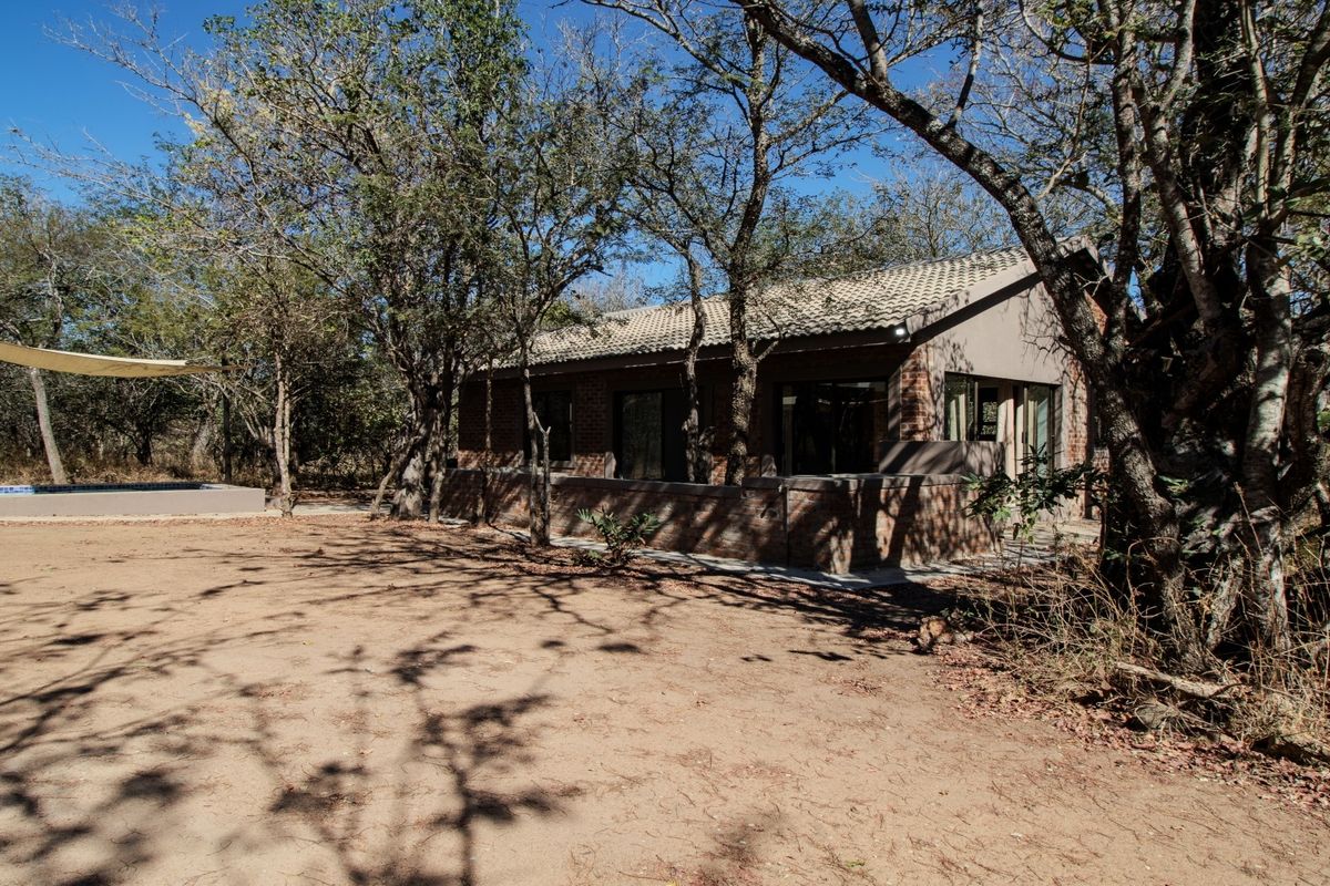 Rear view of a brick house featuring a tiled roof, surrounding trees, and a swimming pool with a shade sail in a natural setting.