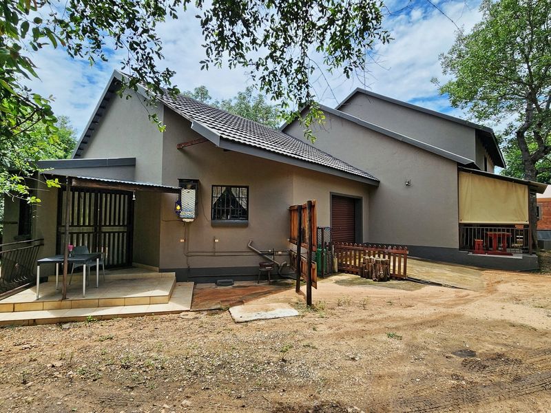 Rear view of the property featuring a tiled patio area, security features, and a spacious garden setting with mature trees.