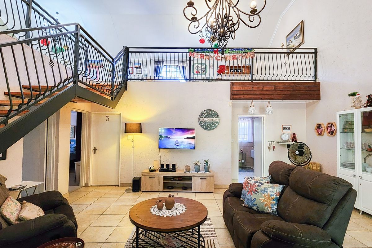 Spacious living room featuring a vaulted ceiling, tiled flooring, and a mezzanine level accessed by a wrought iron staircase.