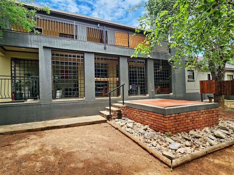 Rear exterior view of a two-story house featuring a brick-built raised platform, metal security grilles on ground floor windows, and an upper-level balcony.