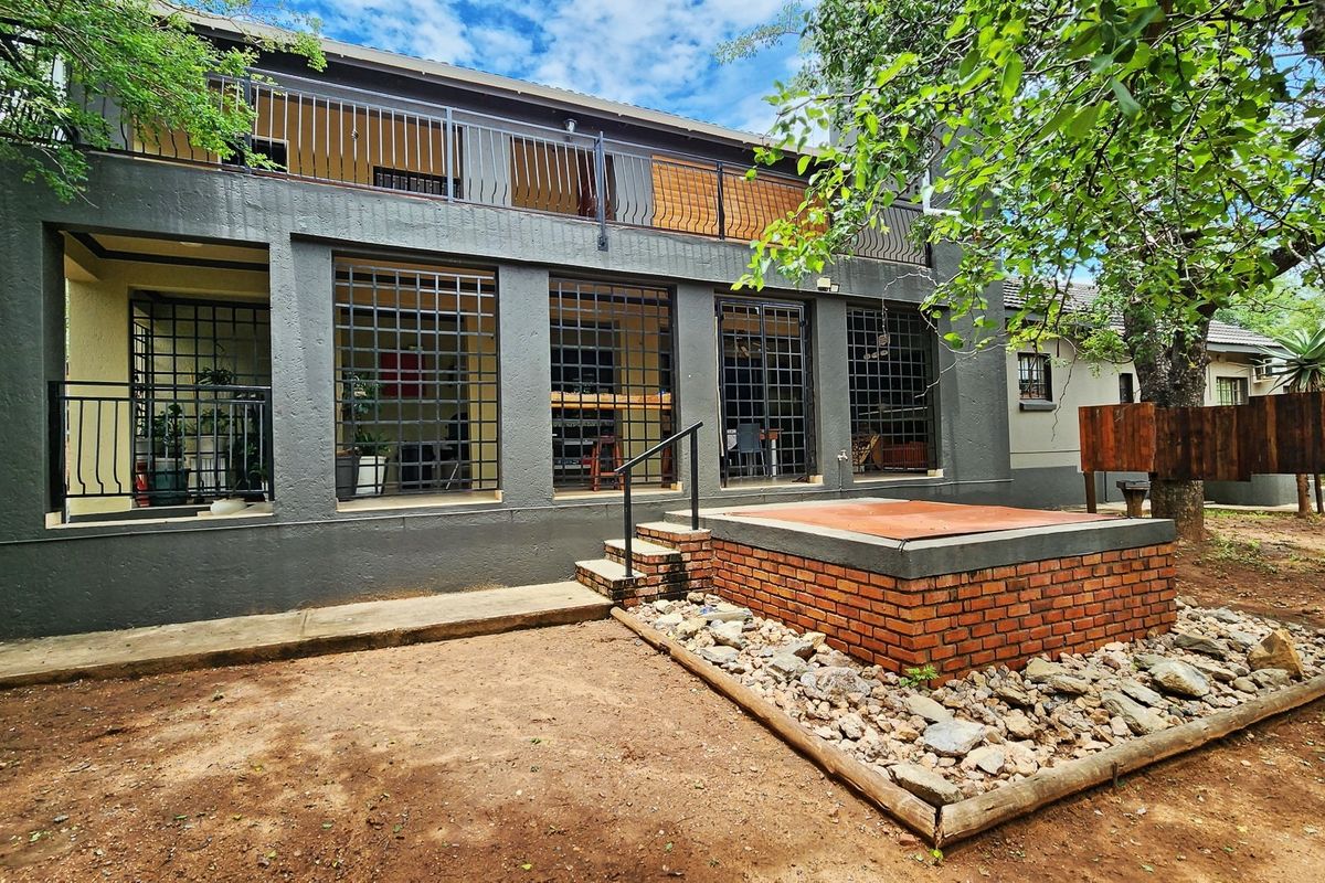Rear exterior view of a two-story house featuring a brick-built raised platform, metal security grilles on ground floor windows, and an upper-level balcony.