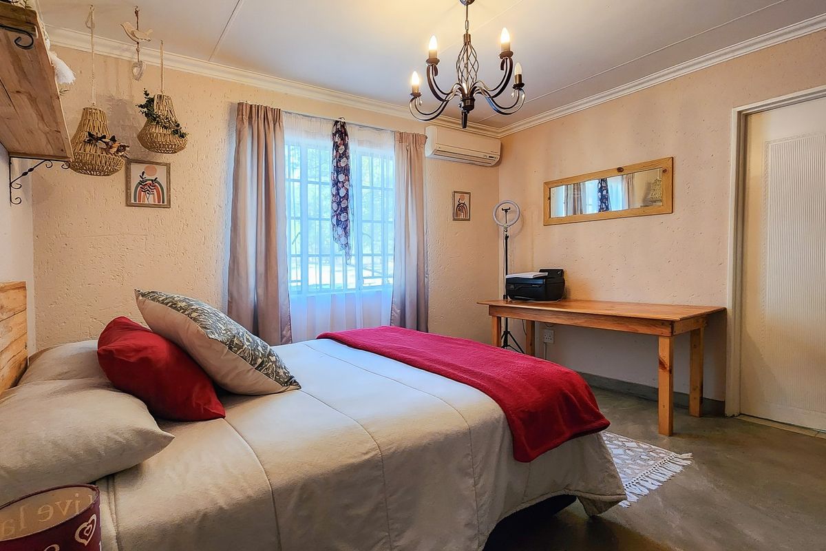 A bedroom featuring textured walls, an air conditioning unit, window security bars, and a classic chandelier light fixture.