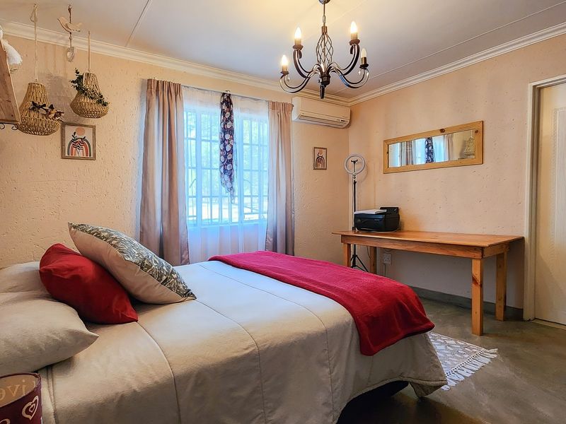 A bedroom featuring textured walls, an air conditioning unit, window security bars, and a classic chandelier light fixture.