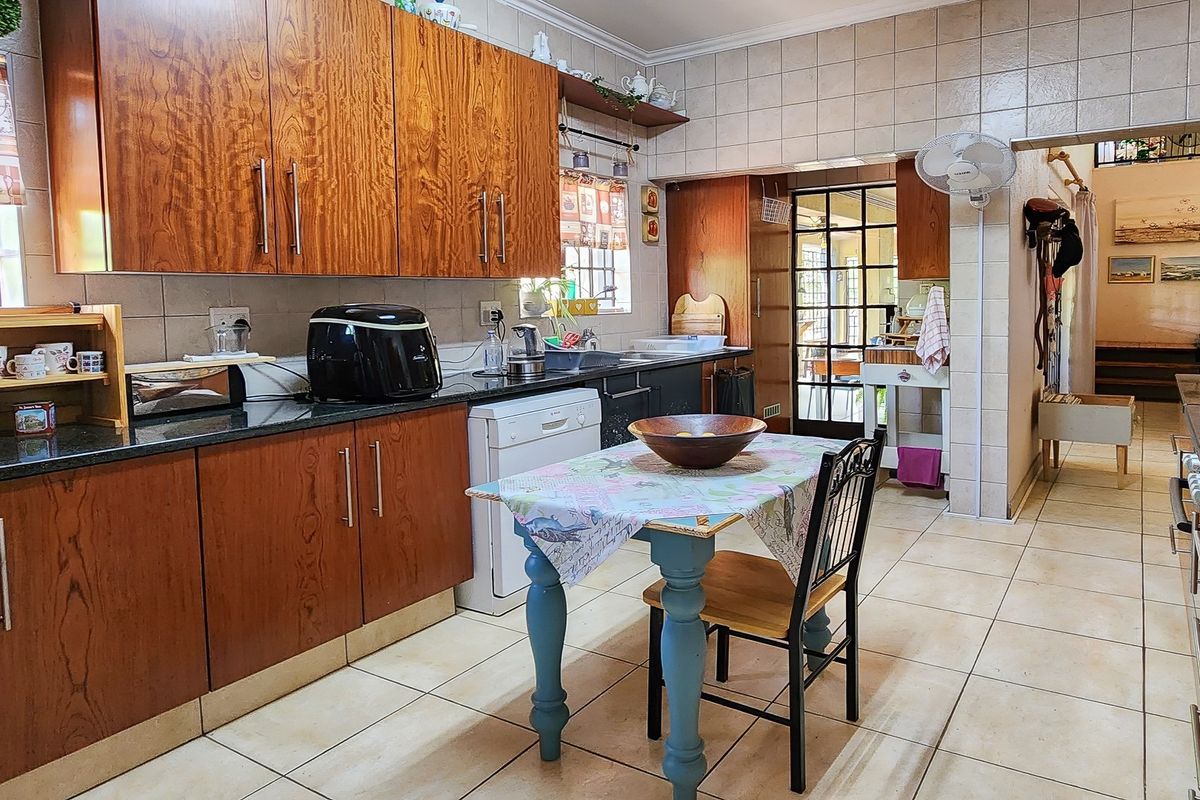 A functional kitchen featuring wooden cabinetry, granite countertops, tiled backsplash, and tiled flooring, with a direct view into the adjacent living area.