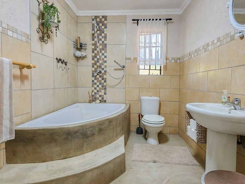 A functional bathroom featuring a built-in bathtub with a step, a pedestal sink, and a toilet, finished with neutral wall tiling.