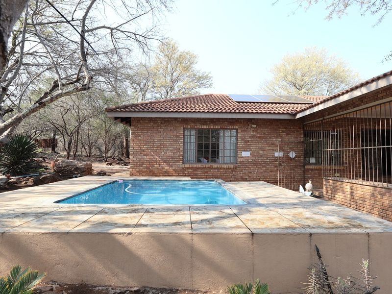A rear exterior view featuring a swimming pool with a tiled deck, set against a face brick house with solar panels installed on the roof.