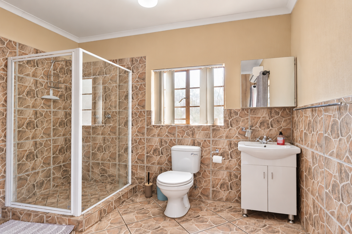 A functional bathroom featuring a glass shower enclosure, a white vanity basin, and distinctive stone-look wall and floor tiling.
