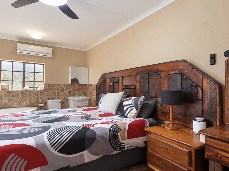 A bedroom featuring an integrated en-suite bathroom area with a built-in bathtub, basin, and stone-style wall tiling, complemented by a split-system air conditioner.