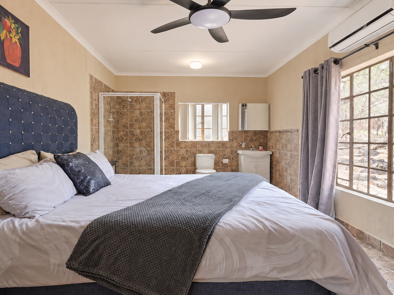 Bedroom featuring an integrated en-suite bathroom with shower, toilet, and vanity, complemented by a ceiling fan and split-system air conditioning unit.