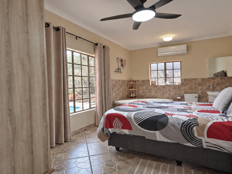 Spacious bedroom featuring an integrated en-suite bathroom, built-in wardrobe, ceiling fan, and split-system air conditioning, with direct access to outdoor views.