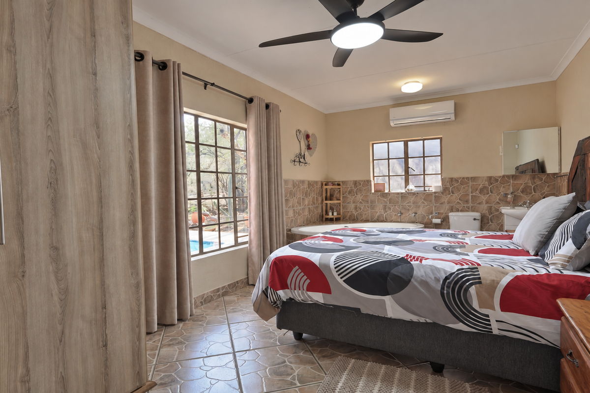 Spacious bedroom featuring an integrated en-suite bathroom, built-in wardrobe, ceiling fan, and split-system air conditioning, with direct access to outdoor views.