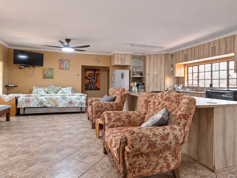 Open-plan living and kitchen area featuring tiled flooring, wood-finish cabinetry, a central kitchen island, and a ceiling fan.