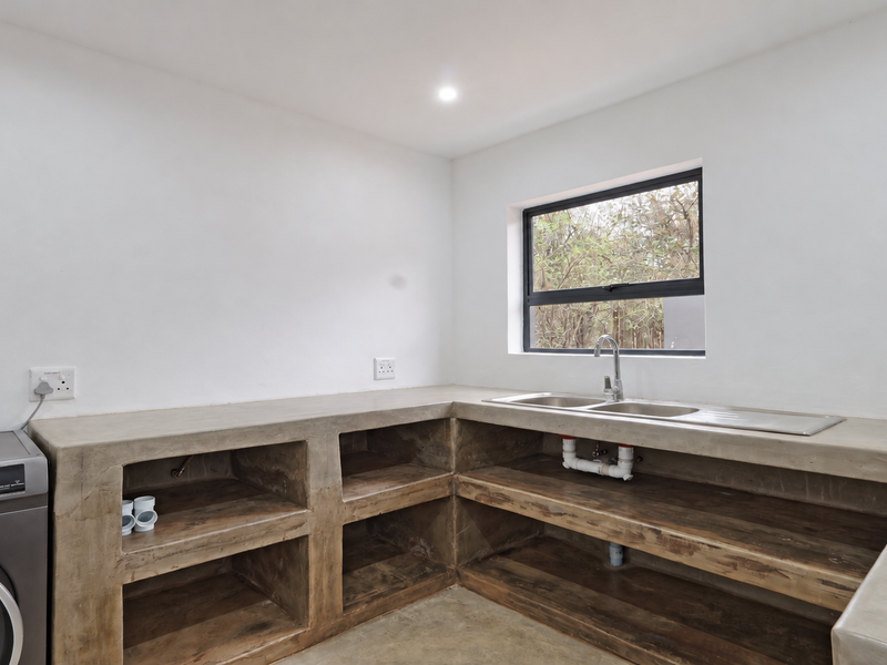 A clean, minimalist laundry room featuring custom concrete countertops, built-in open shelving, and a double stainless steel sink with a modern chrome faucet.