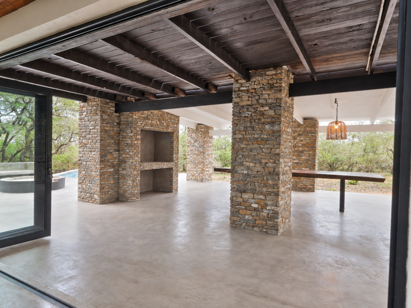 Spacious covered patio featuring stone pillars, exposed timber ceiling, built-in braai, and seamless access to the outdoors through large stacking doors.