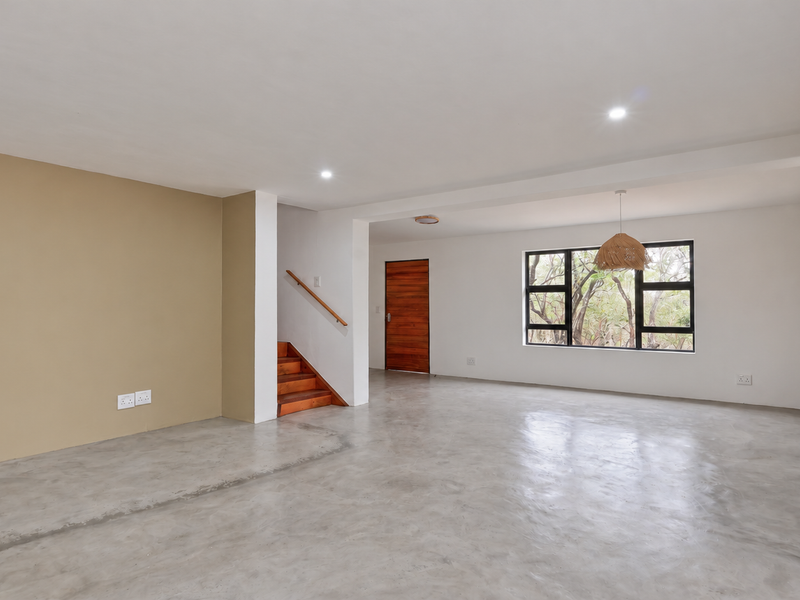 Spacious open-plan living area featuring polished concrete floors, a wooden staircase, and large windows providing natural light and garden views.