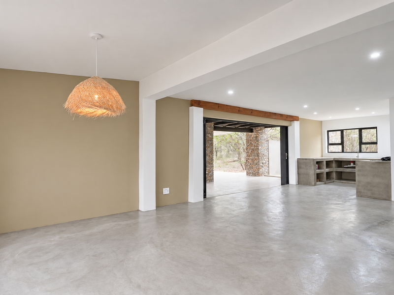 Spacious open-plan living and kitchen area featuring polished concrete floors, built-in concrete cabinetry, and seamless flow to an outdoor patio through bi-fold doors.