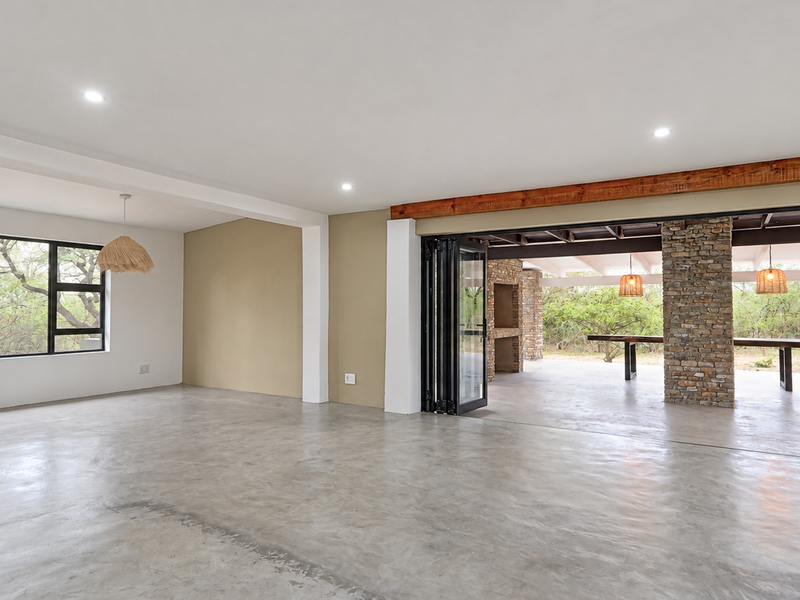 Spacious open-plan living area featuring polished concrete floors, exposed timber beams, and seamless flow to an outdoor patio with a built-in braai.