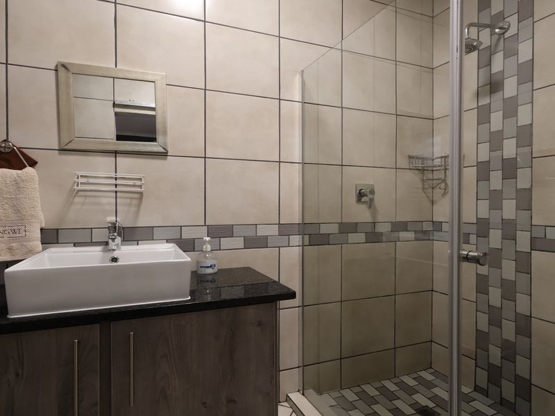 Modern bathroom featuring a vessel sink on a granite vanity, glass-enclosed shower, and neutral wall tiling with a decorative mosaic accent strip.