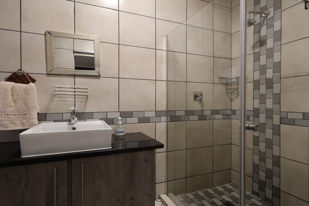 Modern bathroom featuring a vessel sink on a granite vanity, glass-enclosed shower, and neutral wall tiling with a decorative mosaic accent strip.
