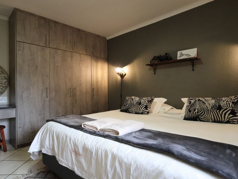 A well-maintained bedroom featuring built-in wooden wardrobes, a matching vanity unit, tiled flooring, and warm wall-mounted lighting.