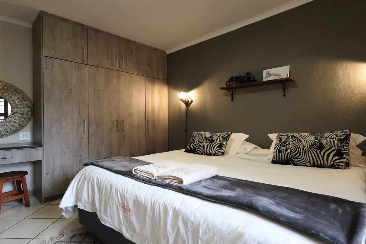 A well-maintained bedroom featuring built-in wooden wardrobes, a matching vanity unit, tiled flooring, and warm wall-mounted lighting.