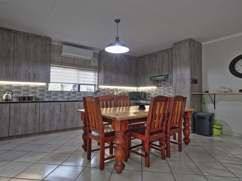 Open-plan kitchen and dining area featuring modern wood-look cabinetry, subway tile backsplash, ceramic floor tiles, and a split-system air conditioner.