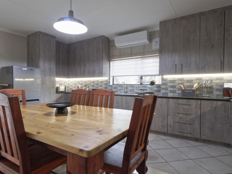 Modern open-plan kitchen and dining area featuring grey wood-grain cabinetry, subway tile backsplash, under-cabinet lighting, and tiled flooring.