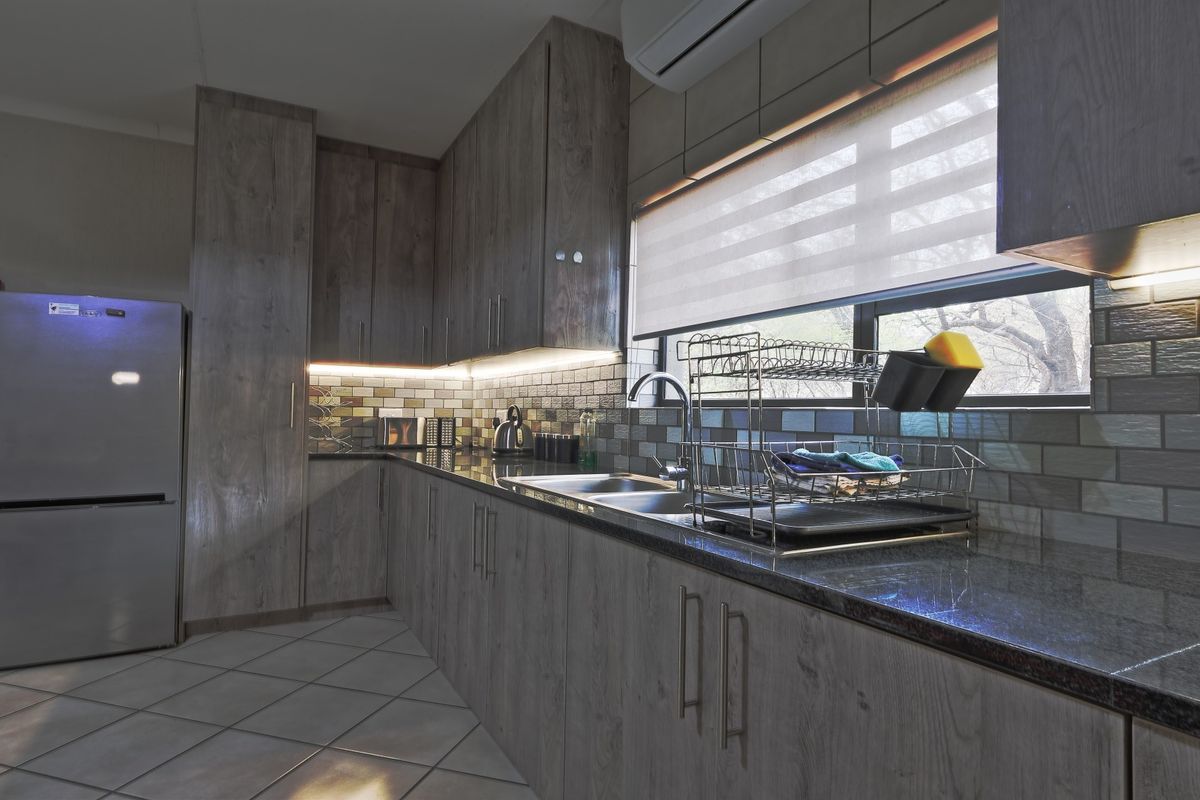 Modern kitchen featuring wood-look laminate cabinetry, granite countertops, a tiled backsplash, and integrated under-cabinet lighting.