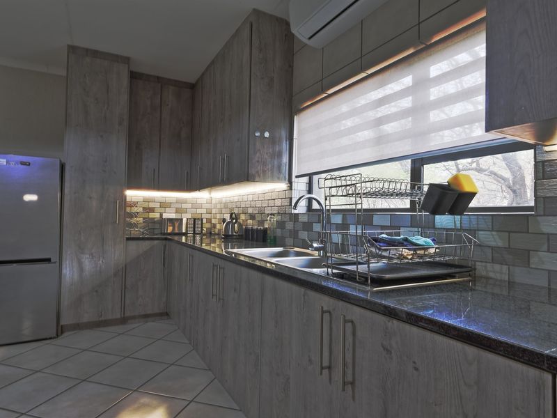 Modern kitchen featuring wood-look laminate cabinetry, granite countertops, a tiled backsplash, and integrated under-cabinet lighting.