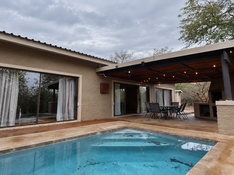 Outdoor entertainment area featuring a swimming pool, covered patio with built-in braai, and large sliding glass doors providing seamless indoor-outdoor flow.