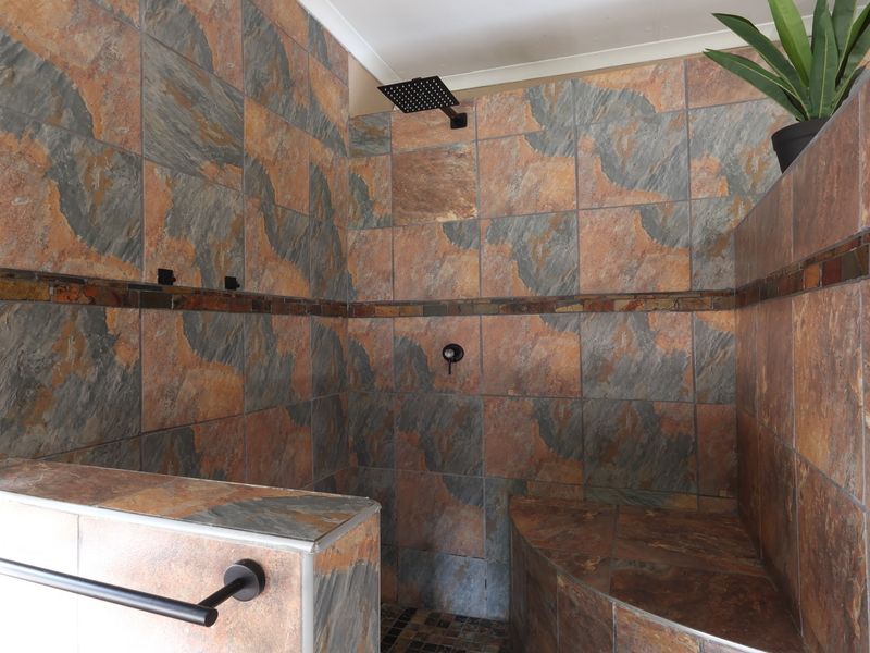 A spacious walk-in shower featuring natural stone-look tiling, a modern rainfall shower head, and a built-in tiled bench seat.