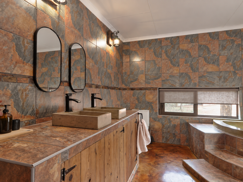 A rustic-style bathroom featuring a double vanity with stone vessel sinks, slate wall and floor tiling, and a sunken bathtub with stepped access.