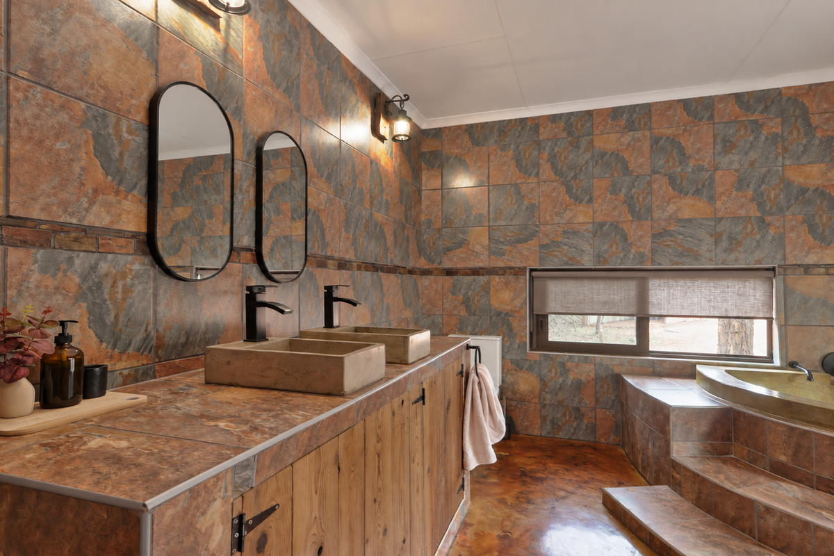 A rustic-style bathroom featuring a double vanity with stone vessel sinks, slate wall and floor tiling, and a sunken bathtub with stepped access.