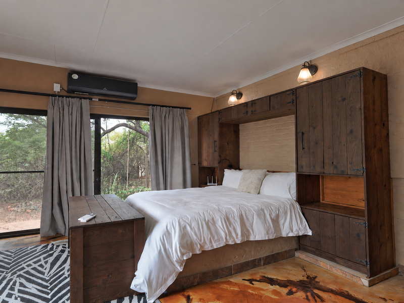 A rustic-style bedroom featuring built-in wooden cabinetry surrounding the bed, polished concrete floors, and a sliding glass door providing access to the outdoors.