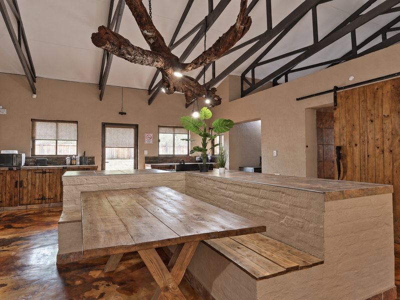 Spacious open-plan kitchen and dining area featuring exposed steel roof trusses, custom brick breakfast bar, and rustic wooden finishes with polished concrete floors.