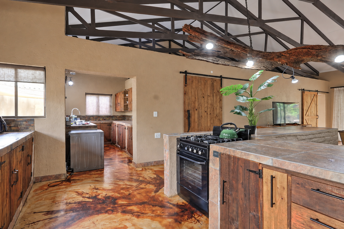 Spacious open-plan kitchen and living area featuring rustic wooden cabinetry, tiled countertops, exposed roof trusses, and unique decorative lighting.