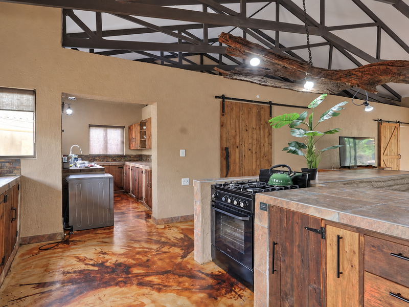 Spacious open-plan kitchen and living area featuring rustic wooden cabinetry, tiled countertops, exposed roof trusses, and unique decorative lighting.
