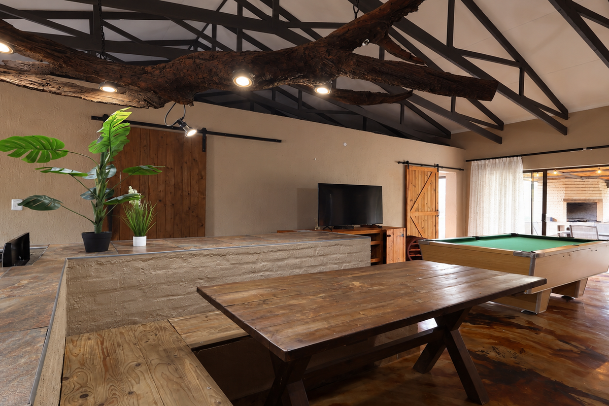 Spacious open-plan living area featuring exposed roof trusses, polished concrete floors, and a unique custom light fixture integrated into a natural wood beam.