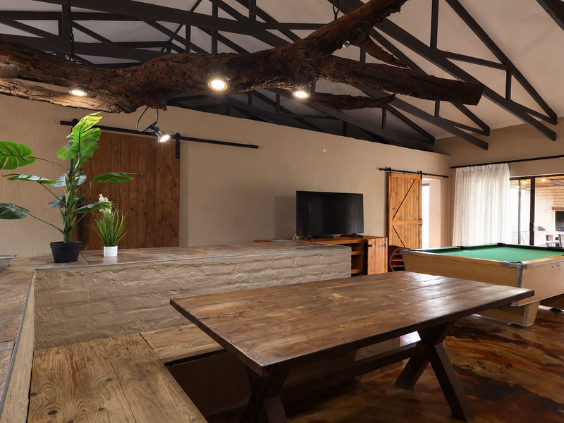 Spacious open-plan living area featuring exposed roof trusses, polished concrete floors, and a unique custom light fixture integrated into a natural wood beam.