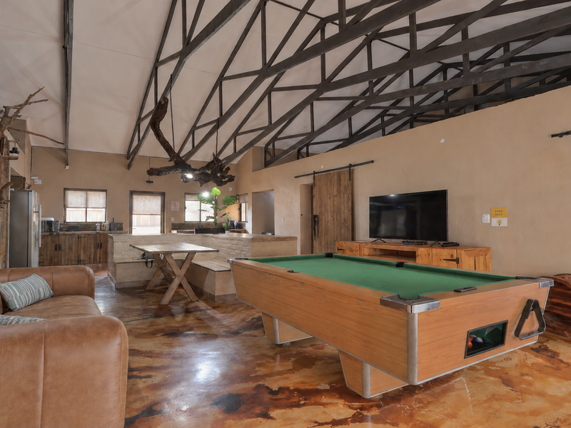 Spacious open-plan living area featuring high vaulted ceilings with exposed steel trusses, polished concrete flooring, and rustic brick wall accents.