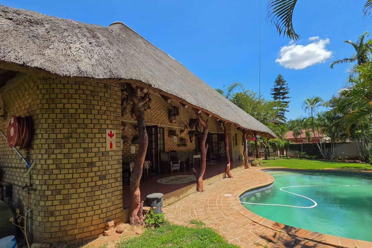 Rear exterior view featuring a thatched roof house, a brick-paved patio area, and a swimming pool set within a landscaped garden.