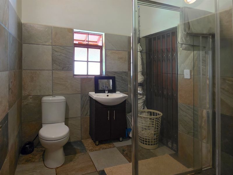 A functional bathroom featuring a shower enclosure, vanity basin, and toilet, finished with natural stone-look wall and floor tiles.